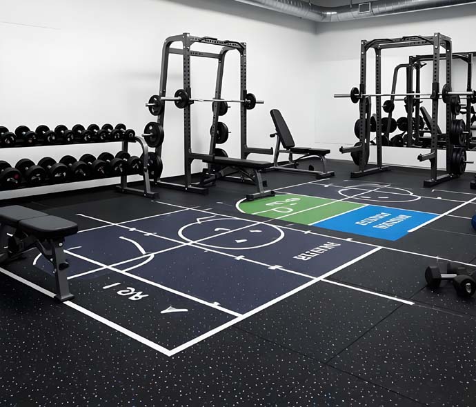 Black speckled rubber gym flooring with marked training zones, power racks, benches and dumbbells in a commercial gym