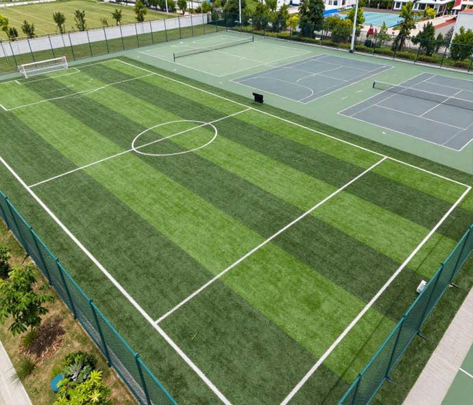 Aerial view of striped green artificial turf sports field with white line markings beside tennis courts and green fencing