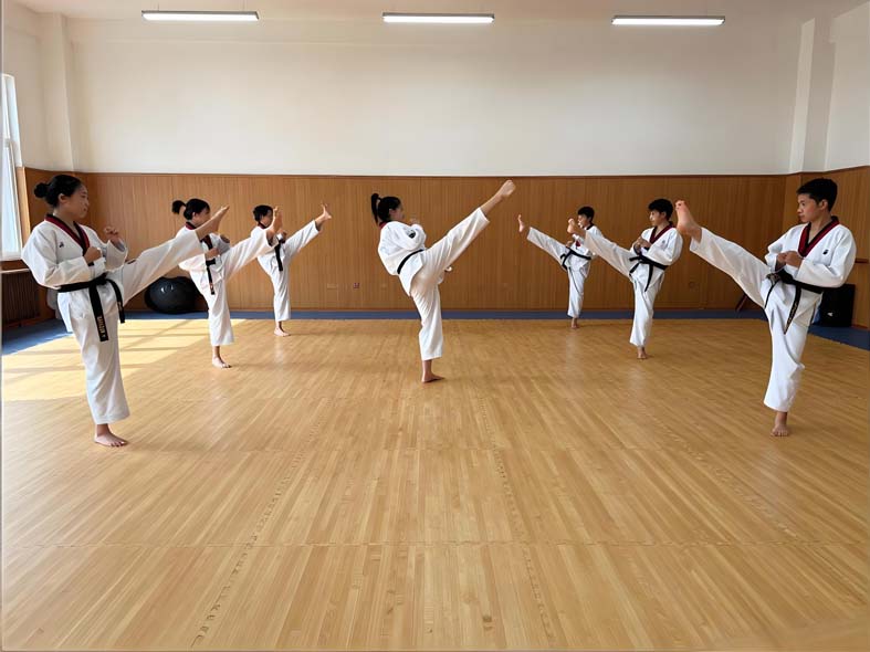 Taekwondo class in white doboks practicing kicks in a line on a wood-grain EVA mat floor in a mirrored dojang