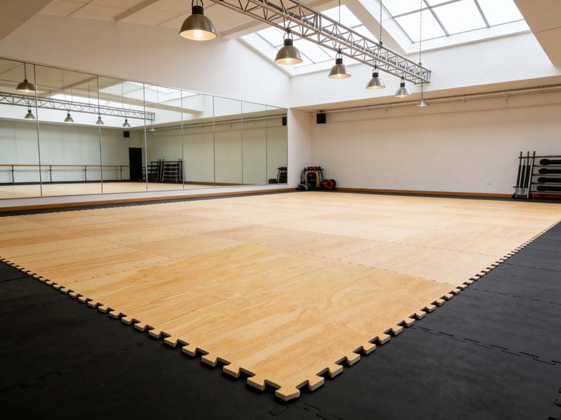 Wood-grain EVA taekwondo mats with black interlocking borders laid across a bright training studio floor