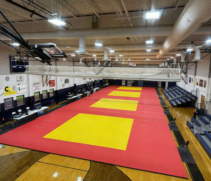 Large red and yellow BJJ and judo mat area laid over a gym basketball floor, set up for a martial arts tournament
