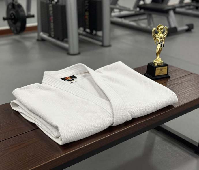 Folded white karate uniform on a wooden bench beside a small gold trophy in a gym