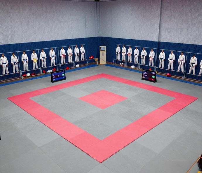 Empty dojo with red and grey mats and rows of white uniforms hanging along the wall