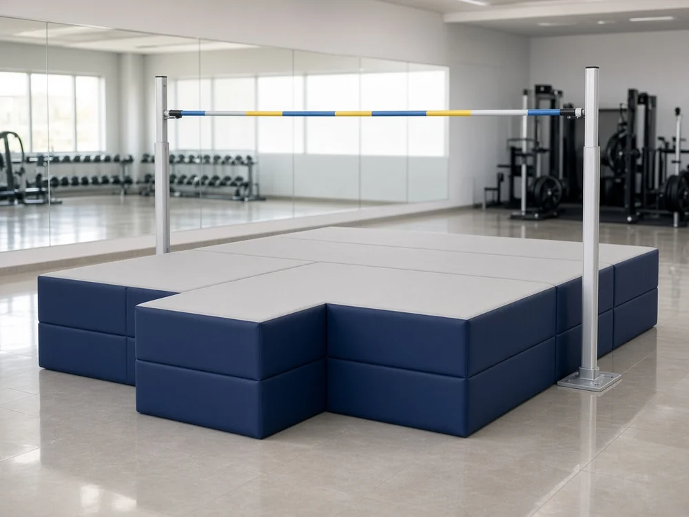 Navy and gray modular high jump landing mat between silver uprights and a banded crossbar in a bright modern gym