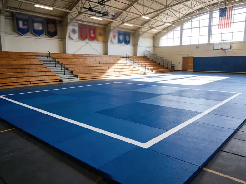 Blue judo mats with white boundary lines installed on the floor of a school gymnasium with wooden bleachers