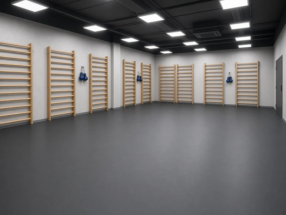 Continuous dark gray MMA mat covering the floor of an empty martial arts gym with wooden stall bars and blue gloves on the wall